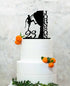 A two-tiered white birthday cake topped with a black silhouette cake topper. The topper features a climber scaling a rock, with the name "JOHNSON" and the number "23" displayed. The cake is adorned with small oranges and green leaves. The background is a textured light color.