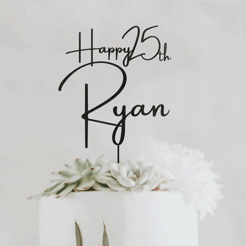 A personalized acrylic cake topper is displayed, featuring the text "Happy 25th Ryan" in an elegant, cursive font. The topper is positioned on a white cake adorned with succulent decorations and white flowers. The background is light and neutral, emphasizing the topper and the cake.