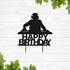 A silhouette of a DJ wearing headphones is shown in front of a turntable setup. Below the DJ, the text "HAPPY BIRTHDAY" is displayed in bold, stylized letters. The image has a light wooden background with green leaves framing the bottom. This cake topper design is suitable for birthday celebrations.