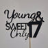 The image features a cake topper made of black glitter cardstock. The design includes the phrases "Young & Sweet" in a flowing script font, with "Only" in a bold, capitalized font. The number "17" is prominently displayed, also in a bold font, indicating a celebration for a 17th birthday. The topper is mounted on a stick for easy placement on a cake, and it is set against a plain background.