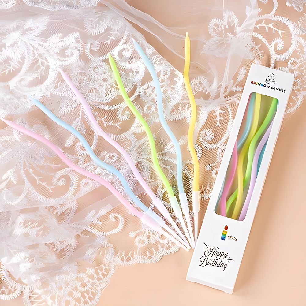 Curved pastel birthday candles in pink, blue, yellow, and green, placed on delicate lace fabric. The white box reads "Happy Birthday."