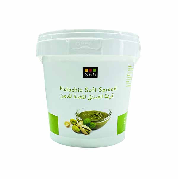 A white container of "Pistachio Soft Spread" with a label featuring the name in English and Arabic. The label includes an illustration of a small bowl filled with the spread and some pistachios beside it. The container has a transparent lid and a green accent at the bottom.