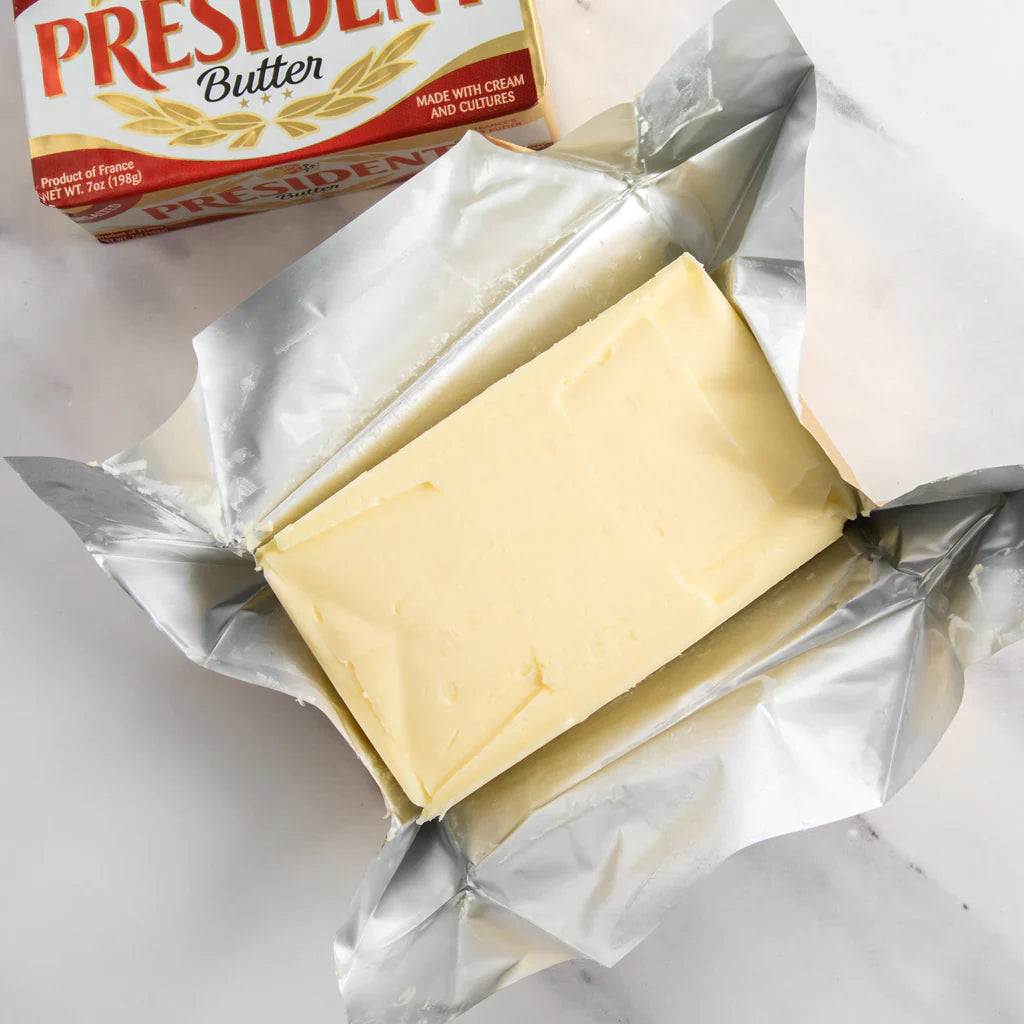 Block of President butter on a white surface with a box of President butter in the background.