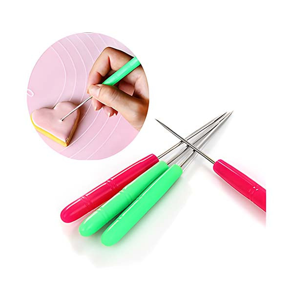 The image shows a set of three scriber modelling tools with colorful handles in pink, green, and a mix of both. The tools have thin metal tips for precise detailing. In the upper left corner, there is a close-up inset showing a hand holding a green scriber tool, used to draw on a pink heart-shaped cookie placed on a light pink surface. The overall composition highlights the tools and their application in cake decorating or cookie design.