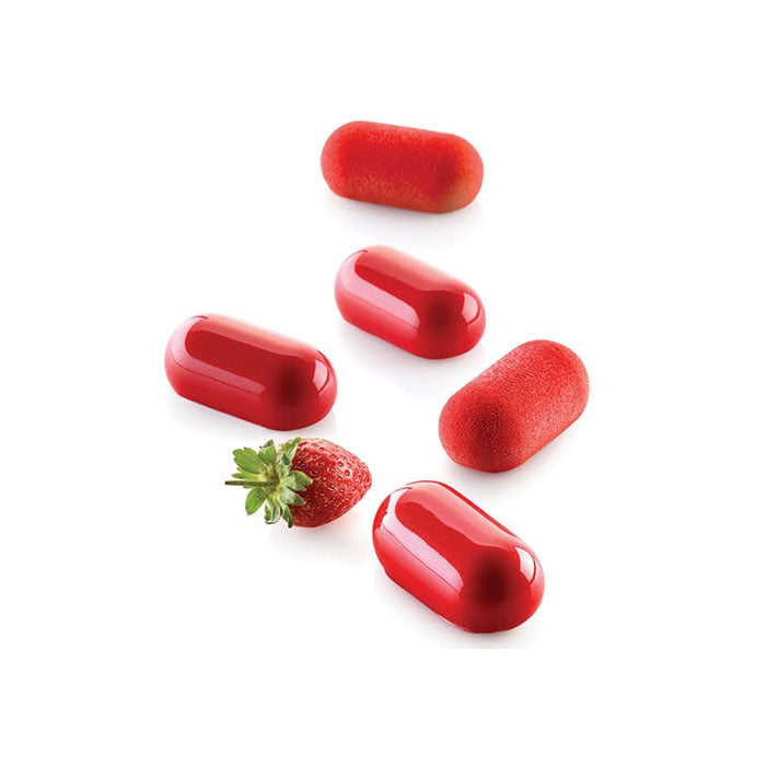 Five red, rounded oval-shaped treats are arranged on a white surface, alongside a fresh green strawberry. The treats vary in texture, with some having a glossy finish and others appearing softer or matte. The overall scene is bright and visually appealing, highlighting the vibrant colors and shapes.