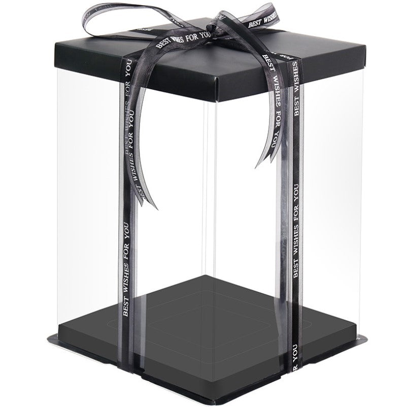 A square tall cake box made of clear PVC material with a black base. The box is topped with a black lid and features decorative ribbons that read "BEST WISHES FOR YOU." The box is displayed with an open design, highlighting its spacious interior.