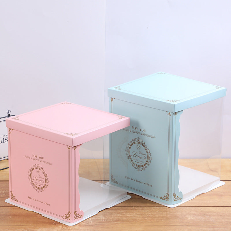 Two square cake boxes with transparent sides, one pink and one light blue. The pink box features decorative gold text that reads "MAY YOU" and "Love&