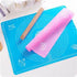 An image of a fondant silicone rolling mat is shown. The mat is bright blue and features printed measurements and design markings useful for baking. A pink silicone rolling mat is partially rolled up on top of the blue mat. Next to the mats, there is a wooden rolling pin. The background is neutral and highlights the mats and rolling pin.