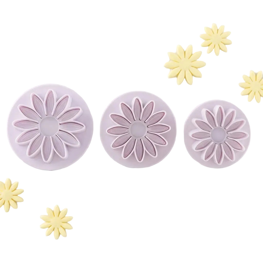 Three purple flower-shaped cookie cutters on a marble surface with yellow flower-shaped cookies.
