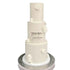 A three-tiered white wedding cake with a smooth finish. The middle tier features the text "MR & MRS" followed by the name "Cameron" in elegant script. The cake is adorned with small white spheres and decorative elements resembling popular sci-fi characters and symbols, such as a stormtrooper helmet and a droid. The cake is placed on a decorative silver cake stand.