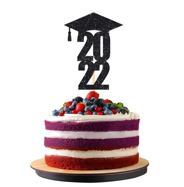 A three-layer cake decorated with vibrant colored layers, including red, purple, and white. The cake is topped with a generous amount of fresh berries, including strawberries, blueberries, and blackberries, along with some green mint leaves. Atop the cake is a black glittery graduation cap and the year "2022" in bold text, marking a graduation celebration. The cake is presented on a round wooden board against a plain white background.