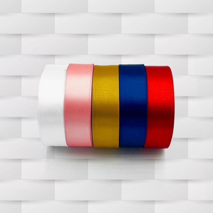 A collection of satin ribbon rolls displayed horizontally on a light gray textured background. The ribbons are arranged from left to right in the following colors: white, light pink, gold, blue, and red. Each ribbon is approximately 2.5 cm in width and the total length is 36 yards.