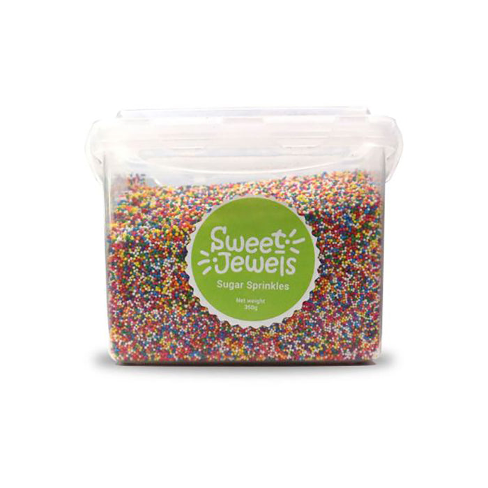 The image shows a clear plastic container filled with colorful confetti sugar sprinkles. The container has a round green label that reads &quot;Sweet Jewels&quot; and &quot;Sugar Sprinkles&quot; along with &quot;Net weight 350g.&quot; The sprinkles are multicolored, featuring a mix of red, blue, yellow, and green, creating a vibrant appearance.