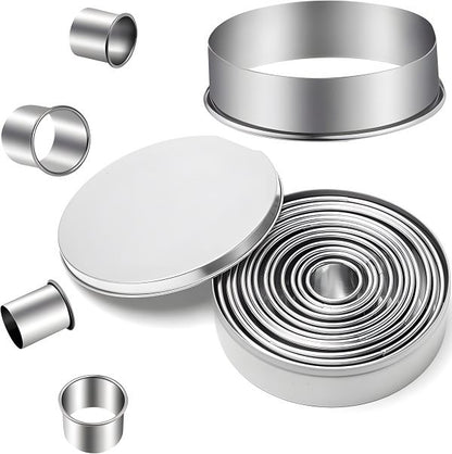 A set of 12 stainless steel round cookie cutters neatly stacked and arranged inside a compact iron storage box. Individual cookie cutters of varying sizes are displayed around the box to showcase the range of diameters.