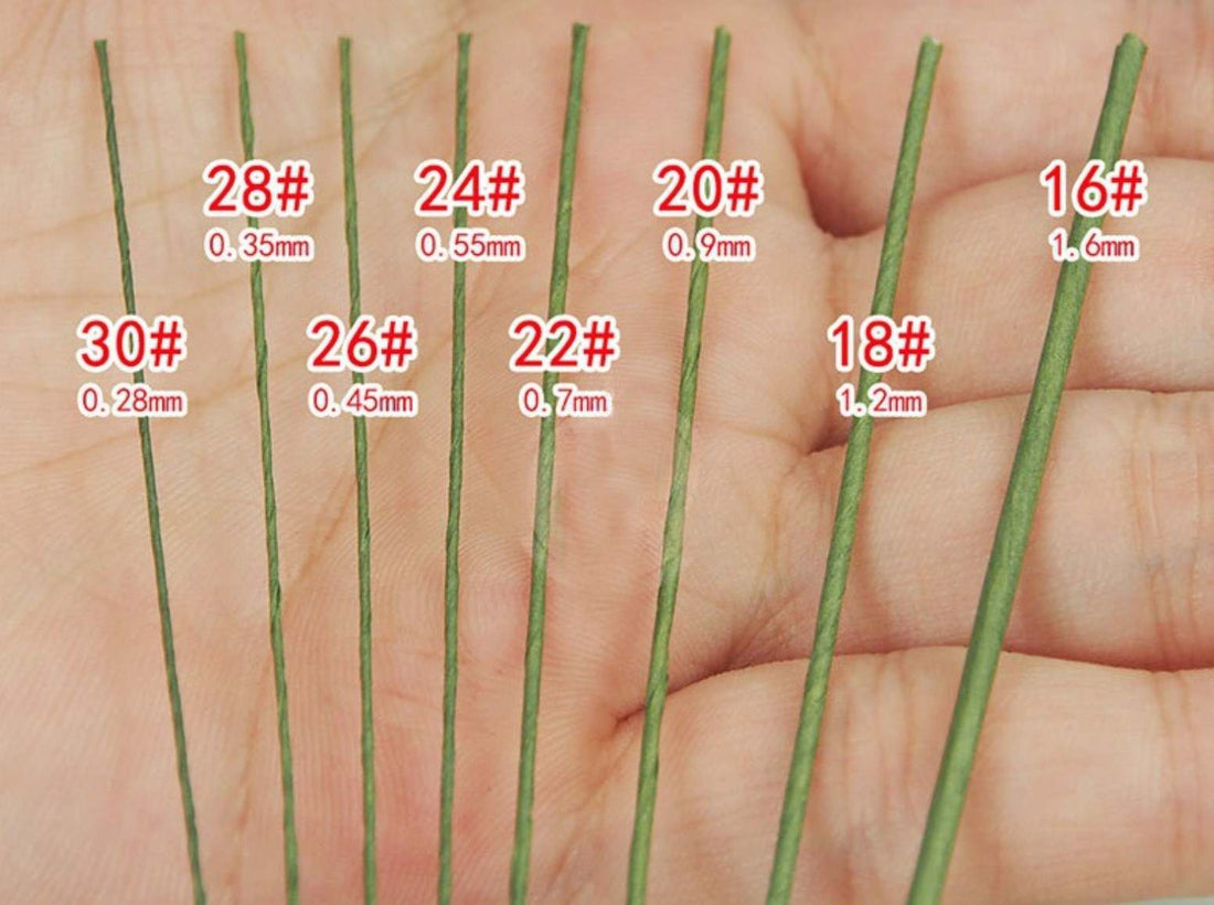 A hand holding several green floral wires arranged in a row. Each wire is labeled with its number (