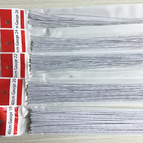 The image shows several packages of white floral wire laid out neatly. Each package contains multiple pieces of wire of various gauges, specifically labeled with their measurements. The top of each package displays a red label indicating the gauge size, which includes gauges 18, 20, 22, 24, and 26. The wires are all the same length, approximately 40 cm, and are neatly organized for easy access.