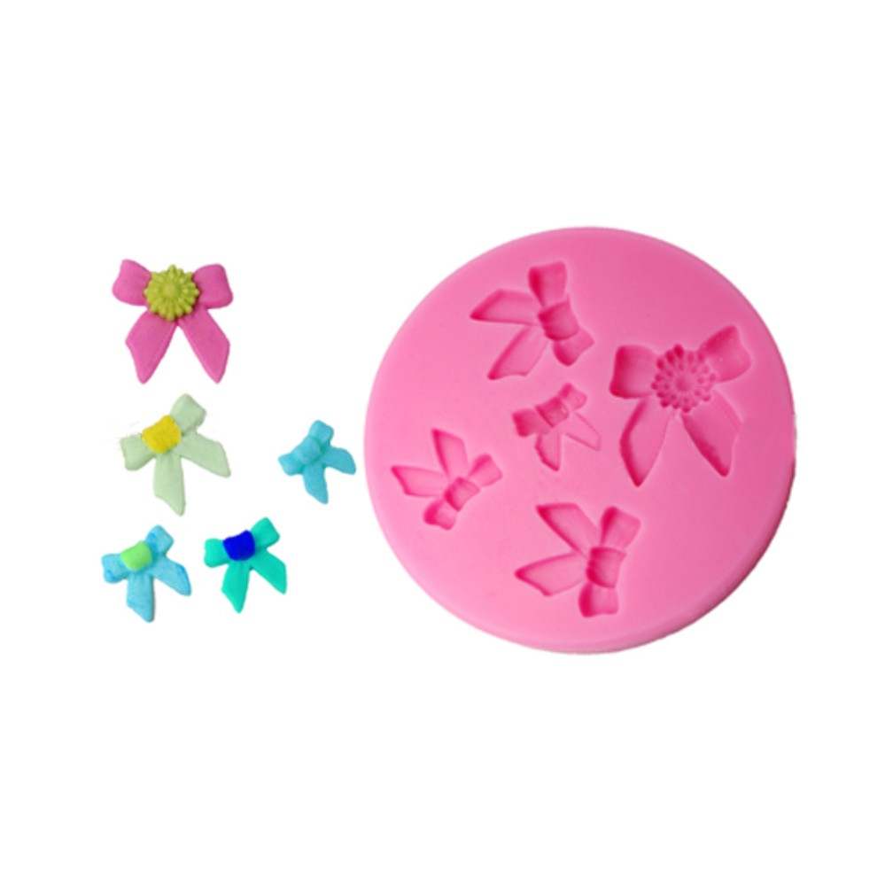 The image features a pink silicone mold shaped like a circle, with several bow-shaped impressions in various sizes. Surrounding the mold are multiple small decorative bows made of colored material, including pink, green, and blue shades. The bows vary in size and design, showcasing different color combinations and embellishments, adding a playful and decorative touch.