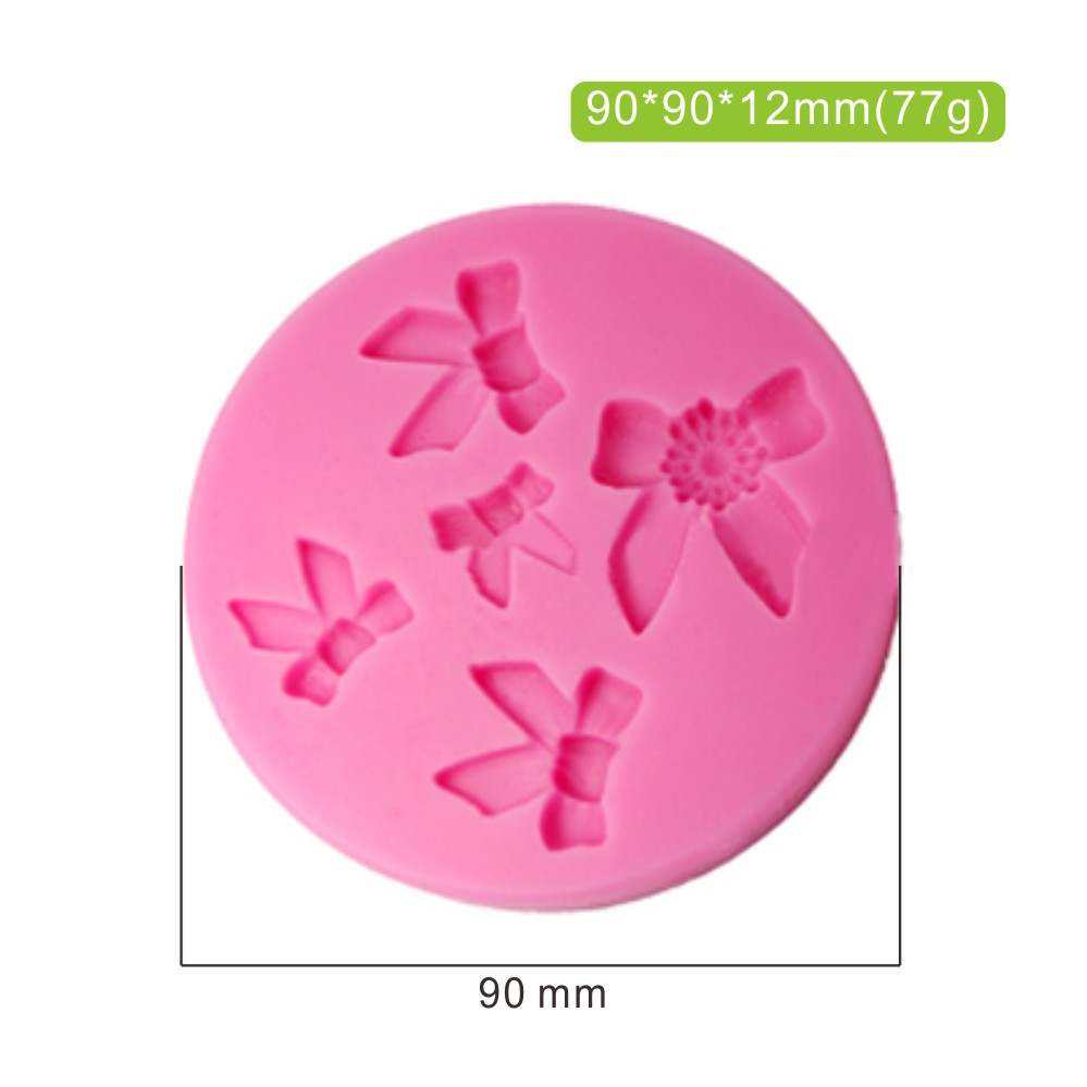 A pink silicone mould featuring five small bow shapes and a floral design in the center. The mould is round with a diameter of 90 mm and a thickness of 12 mm, weighing 77 grams. The dimensions are displayed in the top corner.