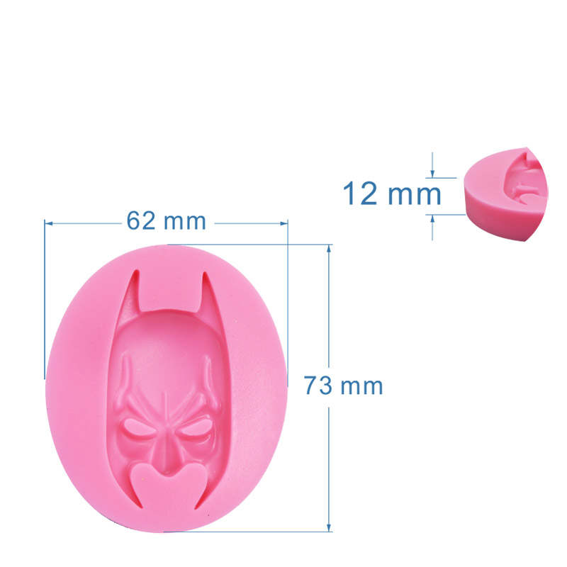 An image of a pink silicone mold shaped like a stylized Batman face. The mold is oval and measures 62 mm in width, 73 mm in height, and 12 mm in depth. Dimensions are displayed next to the mold for reference. A small piece of the mold is shown separately to indicate its detail.
