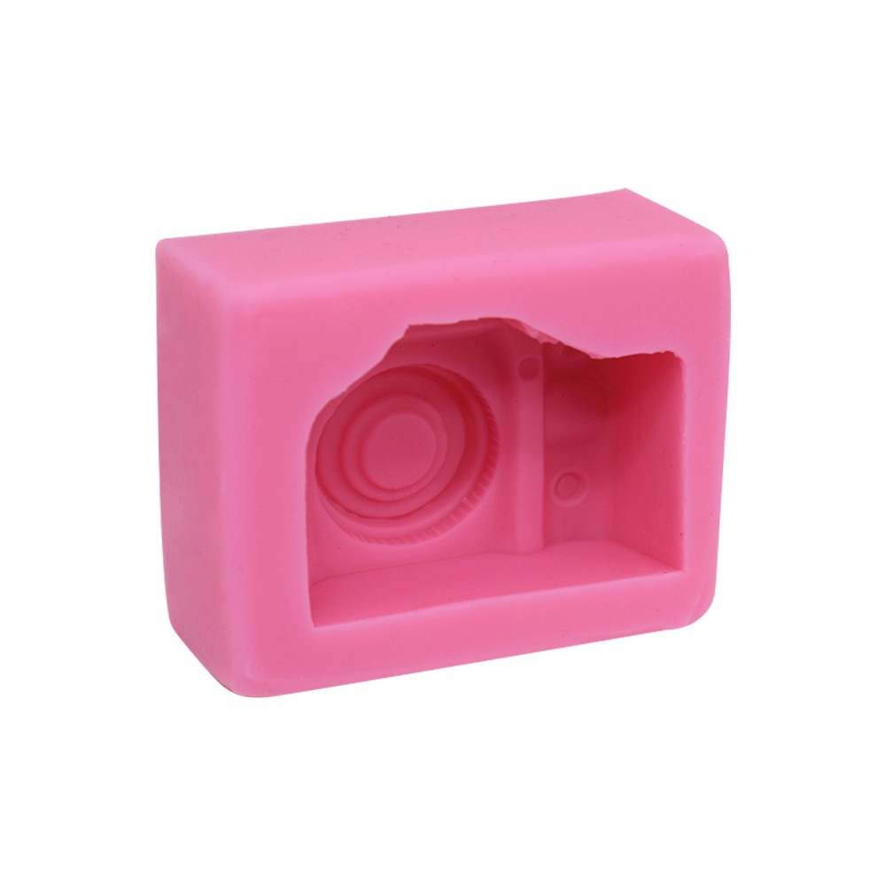 A pink silicone mold shaped like a camera. The mold features an impression of a camera design, including a circular lens and other camera details, and has a rectangular block shape with slightly rounded edges.