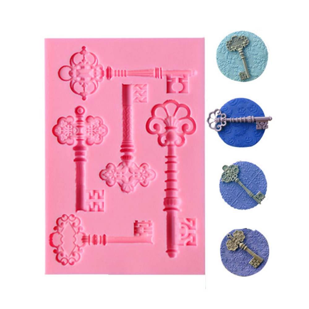 The image features a pink silicone mold designed for creating vintage antique key shapes. The mold displays various key designs, intricately detailed and arranged in different orientations. Alongside the mold, there are several colored impressions of keys, showcasing finished products in light blue, dark blue, and a metallic color. The overall composition highlights the mold&