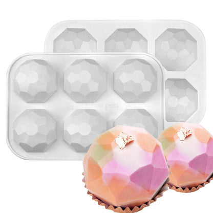 The image shows two silicone molds designed for creating small diamond-shaped balls. There are two trays positioned one behind the other, each featuring multiple geometric cavities shaped like diamonds. In front of the trays, there are two finished silicone molds that have been removed, displaying colorful, faceted balls with a decorative golden topping, resting on brown cupcake liners. The overall color scheme includes pink, orange, and pastel shades.