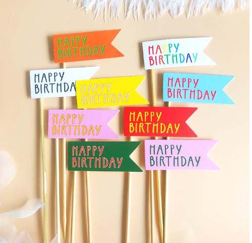 The image features a set of nine colorful cake toppers designed as birthday tags. Each topper consists of a flag with the text "HAPPY BIRTHDAY" written in various colors. The flags are arranged in a visually appealing manner, with a mix of colors including orange, white, yellow, pink, red, and blue. Each flag is attached to a wooden stick, making them suitable for inserting into cakes or desserts for birthday celebrations.