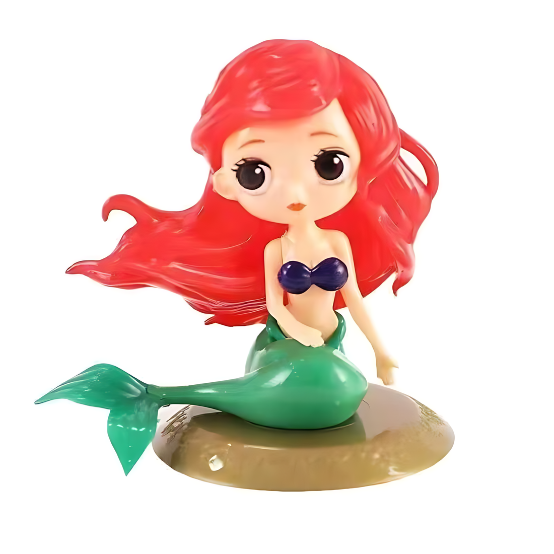 A colorful figurine depicts a mermaid princess with vibrant red hair and large, expressive eyes. She is wearing a blue seashell top and has a green mermaid tail. The figurine is positioned on a round sandy base, giving the impression of an underwater setting. The overall design is cute and whimsical, making it a perfect cake topper for a themed celebration.