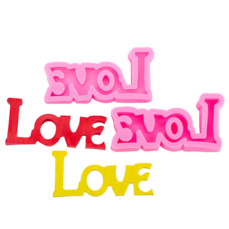 Three silicone molds shaped like the word "LOVE" are displayed in the image. The molds are in various colors: a pink one, a red one, and a yellow one. They feature a playful, stylized font, with the letters appearing thick and slightly rounded. The molds are arranged so that the pink one is at the top, the red one is in the center, and the yellow one is at the bottom. The image is clear, showing the vibrant colors and unique shapes of each mold.