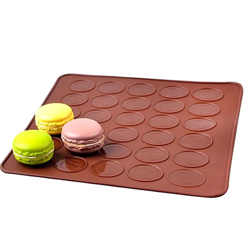 A macaron silicone mat displayed on a flat surface. The mat is brown with multiple circular depressions designed to hold macarons. Three macarons in pastel colors?yellow, green, and pink?are placed on the mat, showcasing their round shape and smooth texture. The background is plain, emphasizing the mat and the macarons.