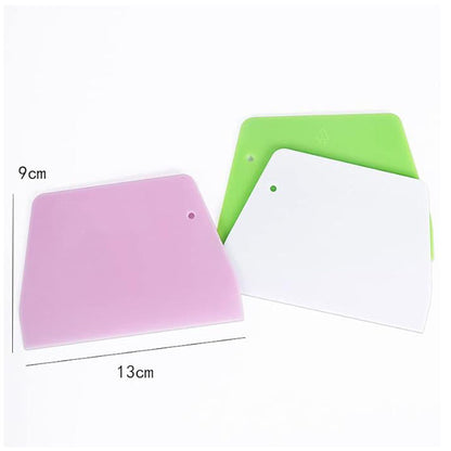 Three plastic dough scrapers in various colors are displayed. The scrapers are arranged with a pink scraper, a white scraper, and a green scraper. Dimensions indicated are 13 cm wide and 9 cm tall. Each scraper has a rounded edge and a hole for hanging.