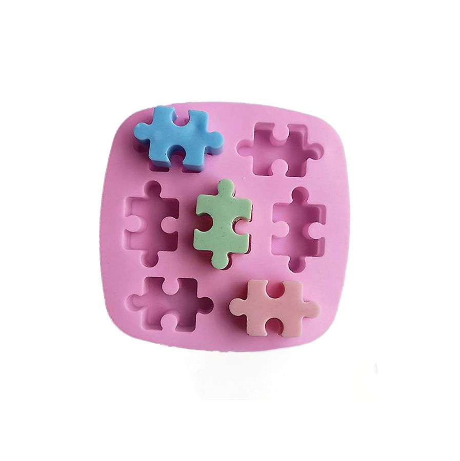 Pink puzzle-shaped silicone mold with three puzzle pieces in blue, green, and pink placed on top. Mold has six empty puzzle slots.
