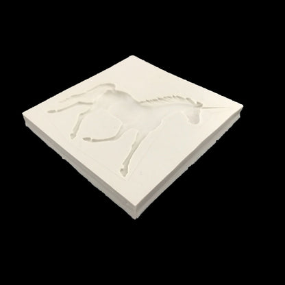 An angled view of a white silicone mold featuring a raised design of a unicorn in a leaping position. The mold is square with clean edges and a smooth surface, designed for creating 3D unicorn shapes in various crafting or baking projects. The background is black, highlighting the mold&
