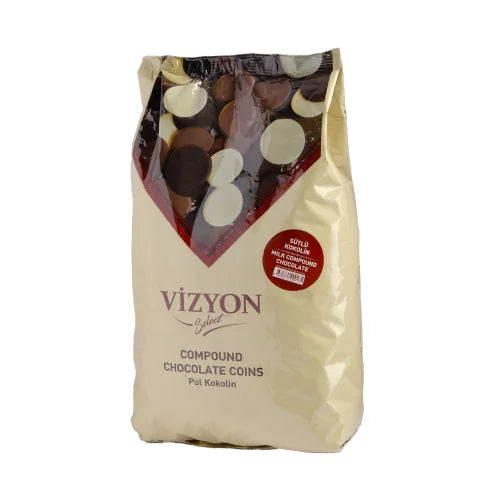 The image features a 2.5 kg bag of &quot;Vizyon Milk Compound Buttons.&quot; The bag is primarily beige with a clear top section displaying various chocolate coins of different colors, including white, milk, and dark chocolate. The brand name &quot;Vizyon&quot; is prominently displayed in bold letters, and there are additional labels indicating that the product consists of compound chocolate coins. The packaging has a modern design with a red and white color scheme.