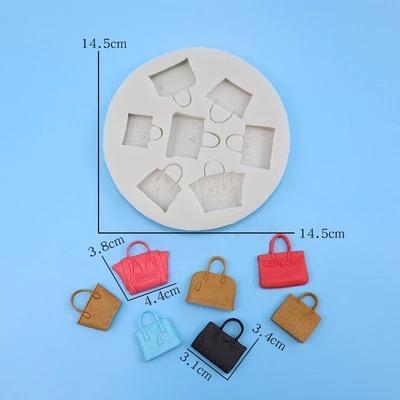 A circular silicone mold with a diameter of 14.5 cm, featuring five handbag shapes of varying sizes. Surrounding the mold are eight small, colorful handbag figurines in red, pink, blue, tan, and black, with sizes ranging from 3.1 cm to 4.4 cm. The background is a light blue color.