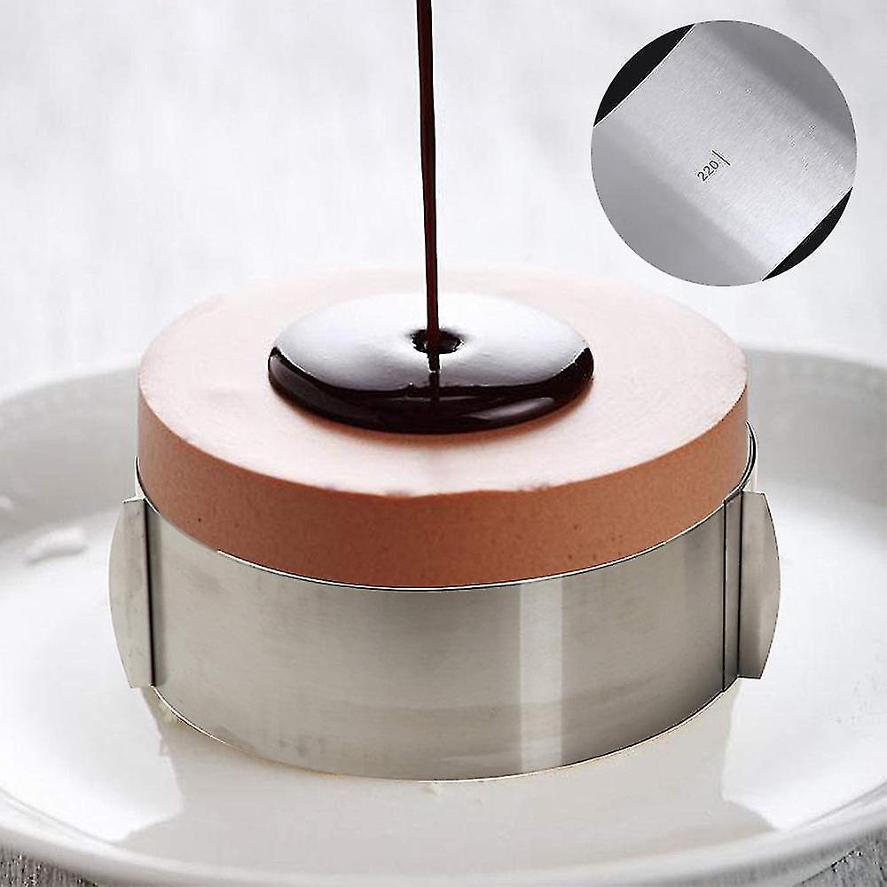 An adjustable round cake ring is placed on a white plate, holding a chocolate mousse dessert. A glossy chocolate sauce is being drizzled onto the top of the mousse, creating a smooth layer. The cake ring is made of shiny stainless steel and features two handles on the sides for easy adjustment. An inset image in the upper right corner shows a close-up of a measurement etched into the metal, indicating a size of 22 cm. The background is softly blurred, emphasizing the dessert.