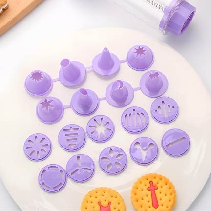 The image features a cookie design imprinting kit displayed on a white surface. The kit includes various purple plastic imprinting tools arranged in two rows. The top row consists of five pointed tips, while the bottom row has eight circular discs with different decorative patterns. In the foreground, there are two yellow cookies with a textured design, one featuring a red decoration.