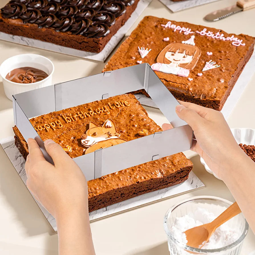 An image showing a pair of hands holding an adjustable square cake ring above a rectangular cake that has &quot;Happy Birthday Love&quot; written on it. The cake is decorated with a cute design of a bear and a small heart. Surrounding the cake are other cakes, a bowl of chocolate, and a bowl of powdered sugar, all on a light-colored tabletop.