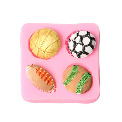 The image shows a silicone mould with four cavities, each shaped like a different type of sports ball. The mould is pink and features a golden basketball, a black and white soccer ball, an orange and brown American football, and a green and brown tennis ball. The mould is designed to create mini treats or decorations resembling these sports balls.