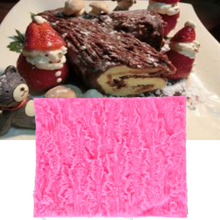The image features a pink silicone mat designed for creating a tree bark texture in fondant or cake decorations. The mat is displayed prominently at the bottom of the image. Above it, there is a festive dessert, resembling a Yule log or rolled cake, decorated with whipped cream and festive figures, including snowmen and strawberries resembling Santa Claus. The surrounding elements suggest a holiday theme, with small decorations of bears and other characters enhancing the presentation.