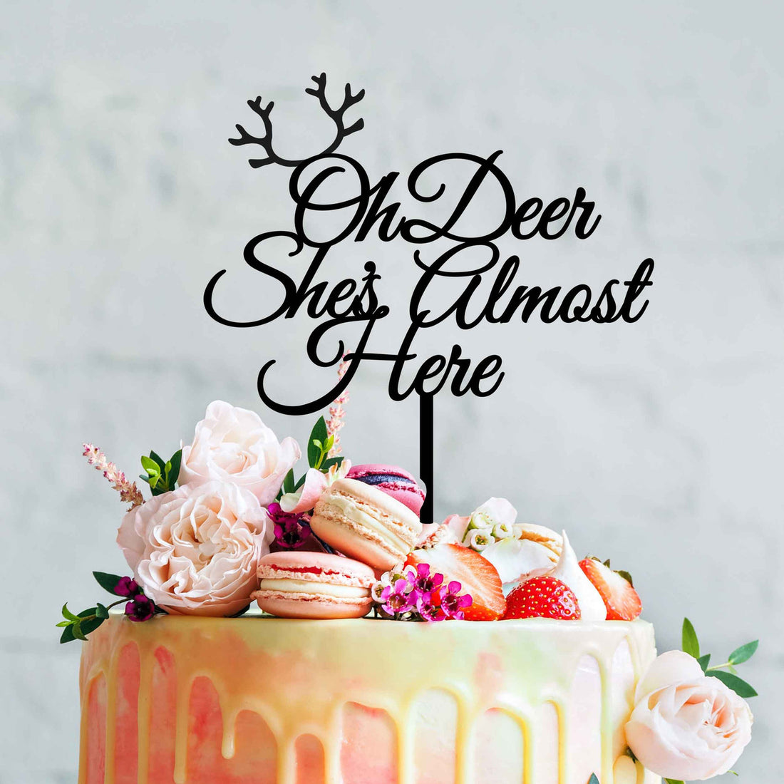 A colorful cake topped with an acrylic cake topper that reads "Oh Deer She&