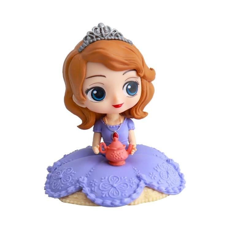 A cute figurine of a princess with long, wavy brown hair and a silver tiara. She is wearing a purple dress adorned with floral patterns. The dress has a textured skirt that resembles fondant or cake icing. The princess is holding a small pink teapot, and her large blue eyes and cheerful expression add to her charm. The figurine is designed to serve as a cake topper.