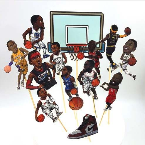 The image features a basketball-themed cake topper set that includes multiple cartoon-style figures of basketball players in various action poses, each holding a basketball. The backdrop depicts a basketball hoop. A prominent sneaker design is positioned at the base among the figures. The scene is colorful and energetic, ideal for celebrating a basketball-themed occasion.