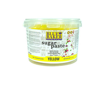 A 1 kg tub of Blue Baker yellow sugar paste (fondant). The tub features a transparent lid and a colorful label. The label includes the product name "BLUE BAKER" at the top, followed by "sugar paste" and indicates the color "YELLOW." Additional information is provided on the label, including ingredients and usage instructions. The overall design is bright and eye-catching, suitable for baking and decorating cakes.
