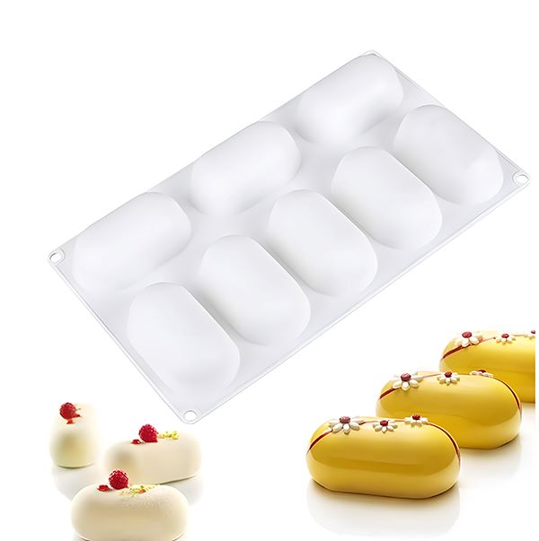 A large white silicone mould designed for making capsule-shaped treats. The mould features eight cavities, can be seen above several finished products that are oblong, shiny, and decorated with small flowers and fruits. The finished treats include a yellow one adorned with a red and white flower and a couple of white ones with berries on top.