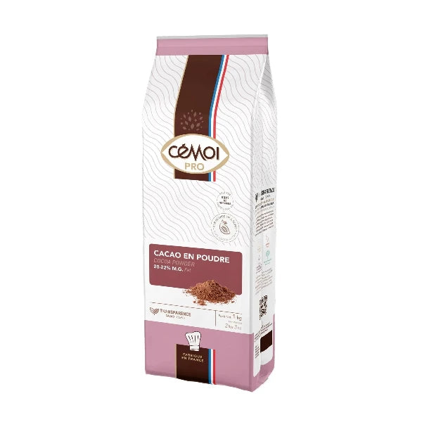 Photo of a 1 kg package of Cémoi Pro cocoa powder with 20-22% M.G. fat, featuring a white background and a detailed product design. The packaging highlights include a brown and pink color scheme, a gold-accented logo, a small pile of cocoa powder, and French branding with a tricolor ribbon motif. The text is presented in both French and English.