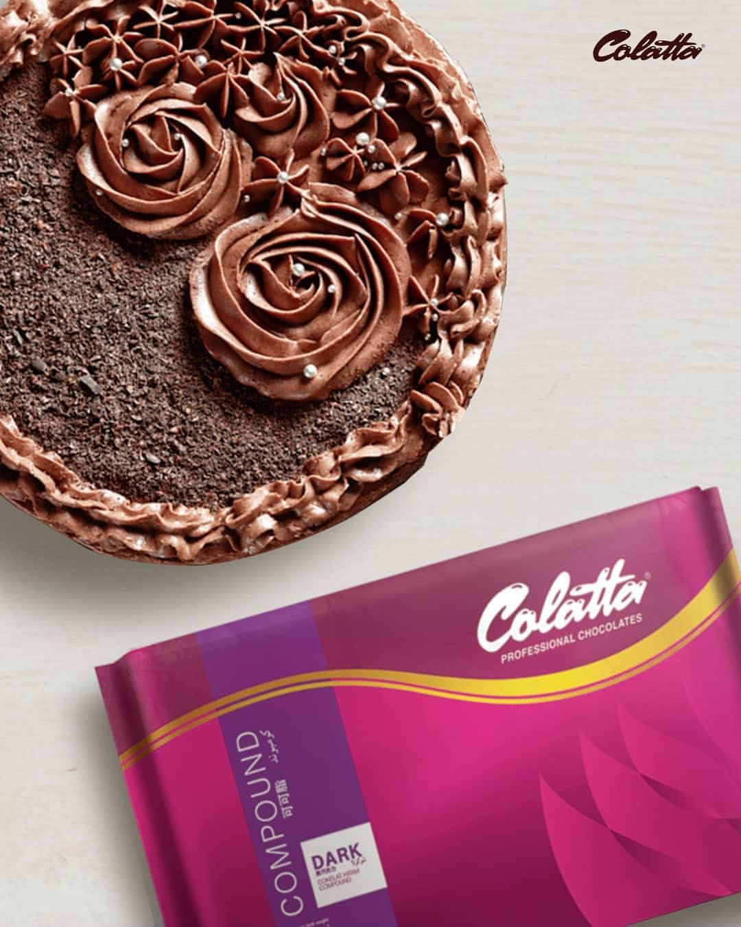 The image features a beautifully decorated chocolate cake with intricate chocolate frosting designs, including rose-shaped decorations and small delicate flowers. The cake is placed on a light-colored surface. Next to the cake, there is a package of &