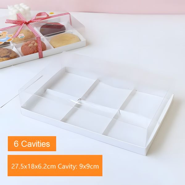 The image shows a clear plastic pastry box designed to hold six portions of donuts. The box is rectangular and features dividers to create six individual cavities. It is displayed on a light background, with a prominent orange label indicating &quot;6 Cavities&quot; along with the dimensions: 27.5 x 18 x 6.2 cm and cavity size of 9 x 9 cm. The lid of the box is slightly open, revealing colorful donuts inside, along with a ribbon tied around the box.