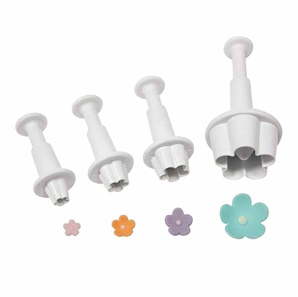 A set of four white plunger cutters in varying sizes, designed to create flower shapes. The cutters have cylindrical handles and flower-shaped cutting edges. Next to them are five finished flower-shaped pieces in pastel colors: pink, orange, purple, and blue, with small rounded centers.