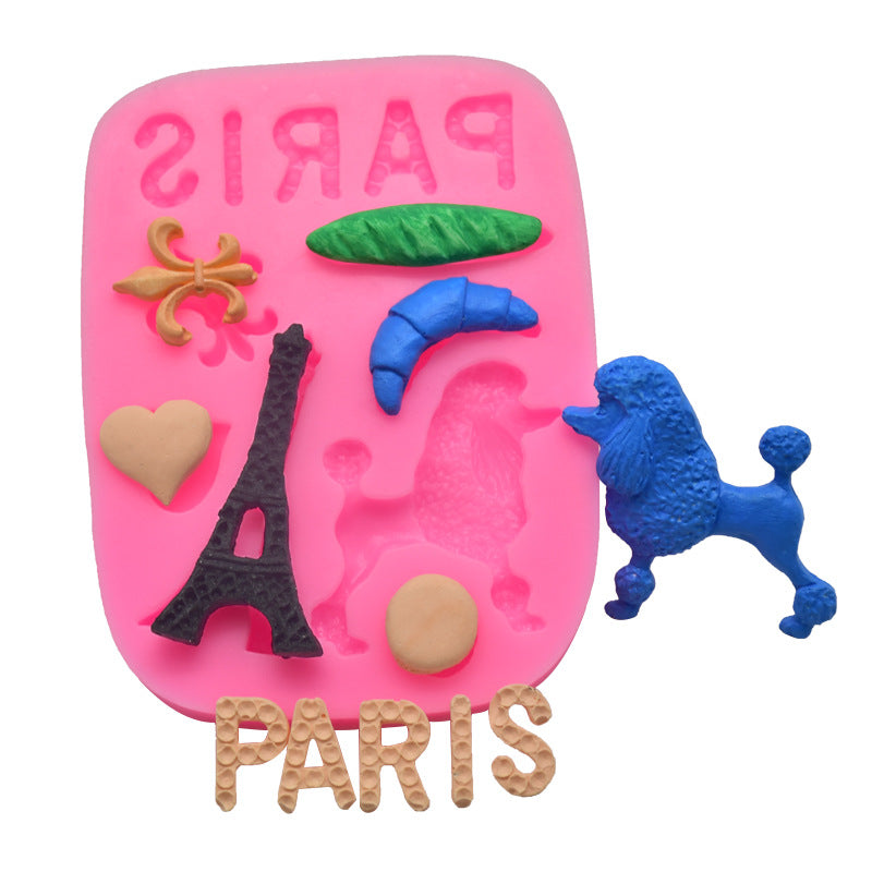 A pink silicone mold designed with various Paris-themed shapes. The mold features the word "PARIS" at the bottom and includes shapes of the Eiffel Tower, a blue poodle, a green leaf, a blue croissant, a heart, and a beige circle. The molded shapes are displayed alongside actual figurines made from the mold.